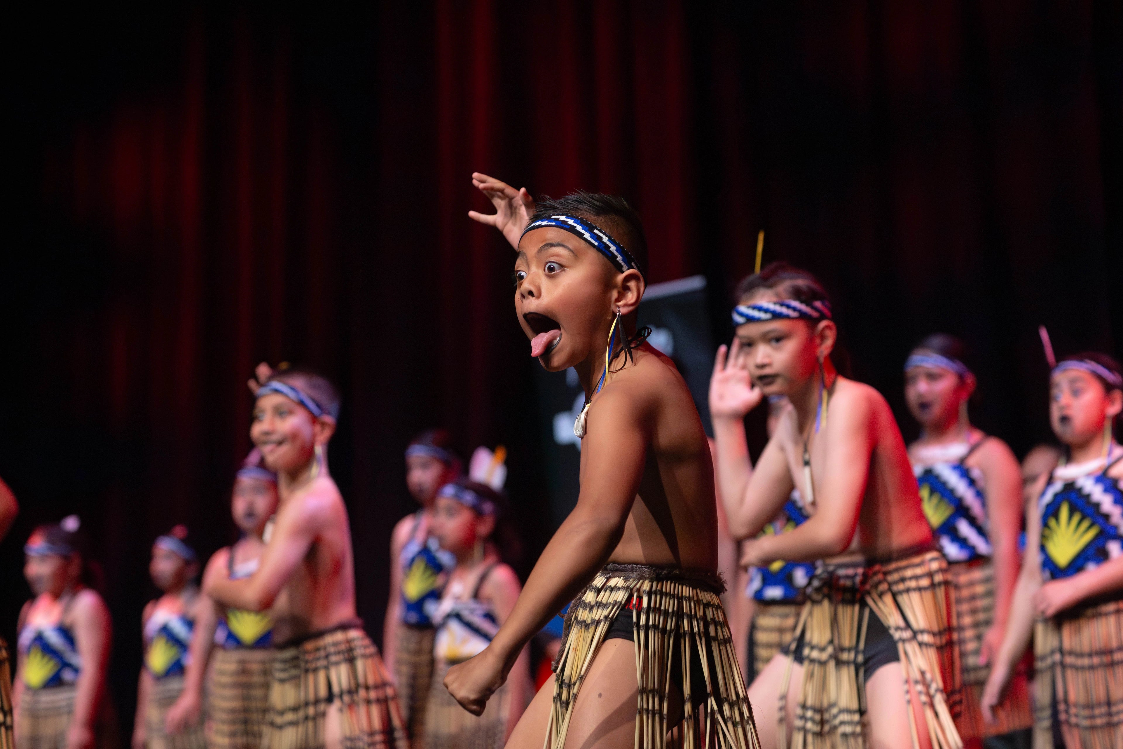 Children in traditional costumes performing on stage with a dark curtain background